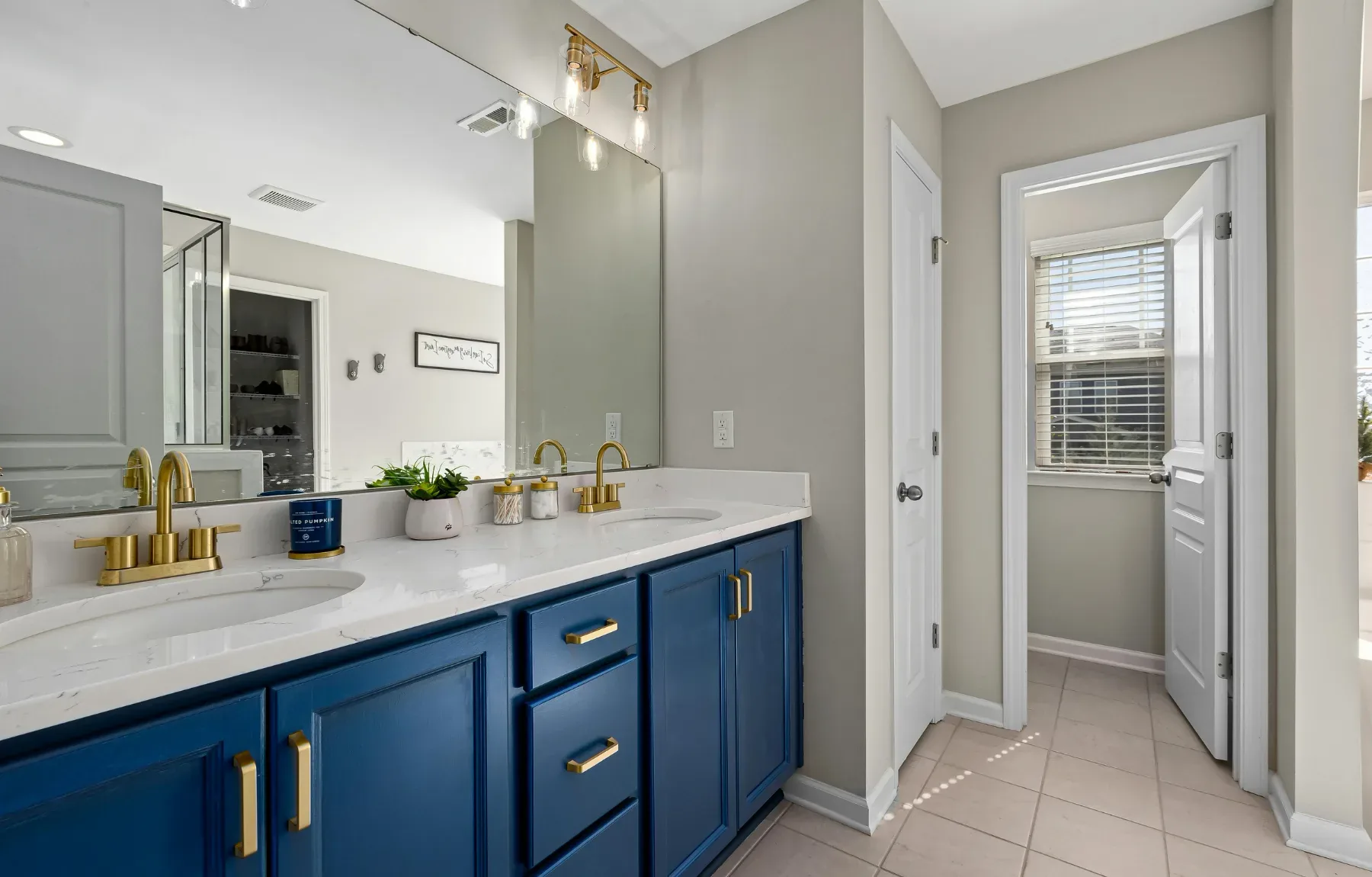 A finished bathroom features a double vanity with deep navy blue shaker cabinets, brass cup pulls, and a white marbled quartz