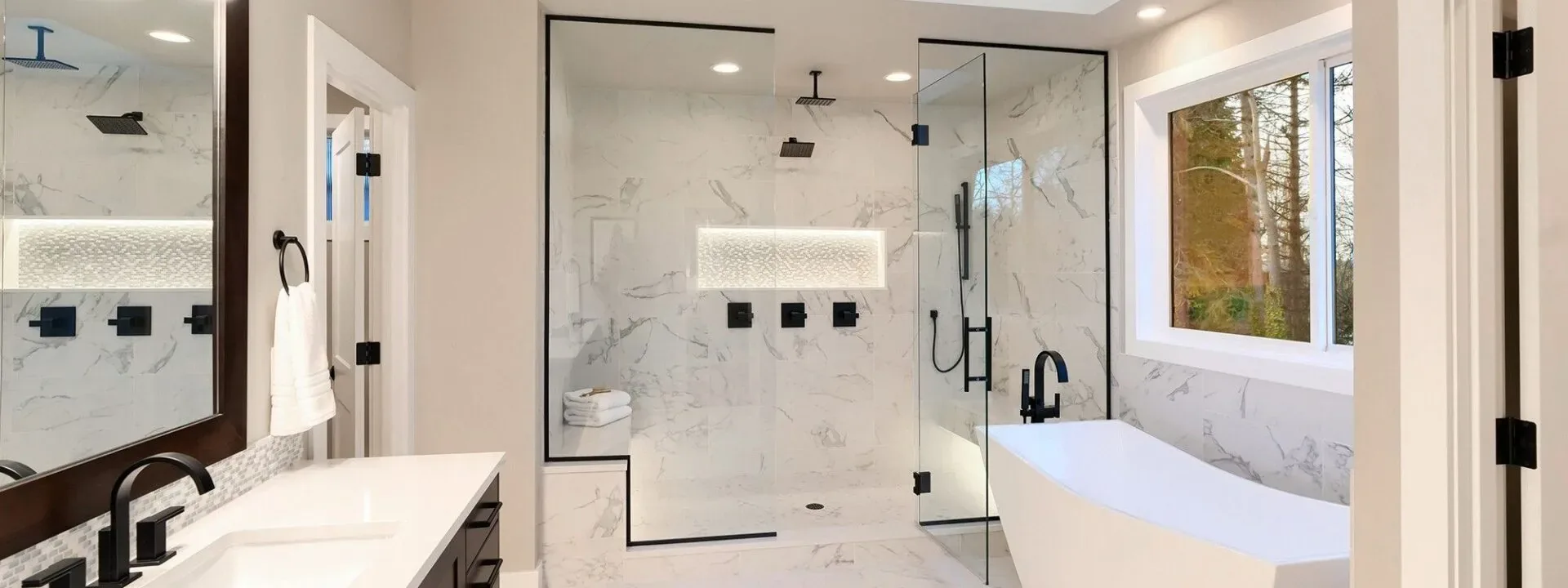 Modern bathroom with marble walls, frameless glass shower enclosure, and soaking tub by window.